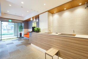 A modern reception area with a wooden counter, a potted plant, and a bench. - Tokyu Stay Yoga (Tokyo)