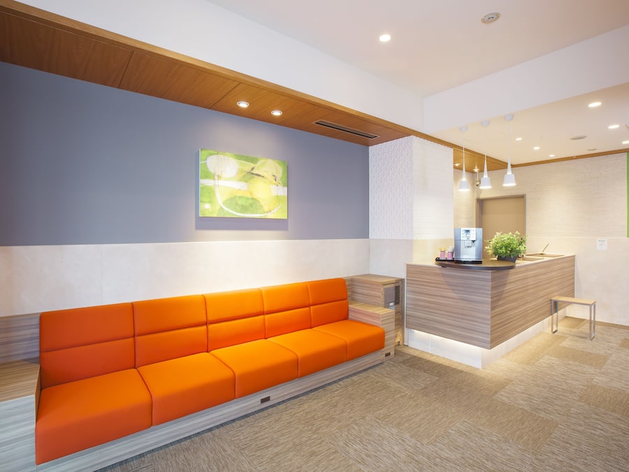 A reception area with a wooden reception desk, a modern orange sofa, and a wall-mounted artwork.