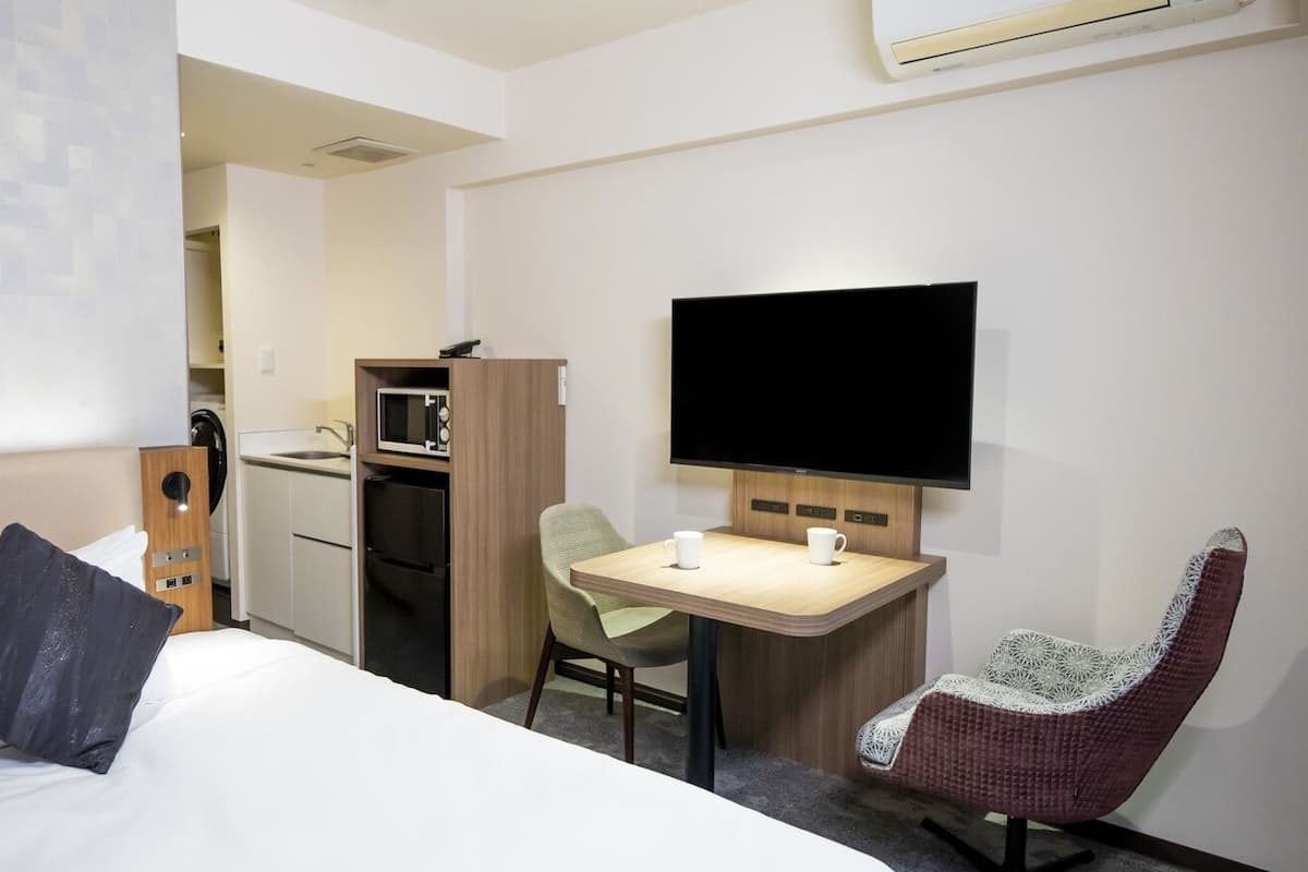Ein Hotelzimmer mit Bett, Schreibtisch, Stuhl, Fernseher und einer Küchenzeile.