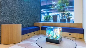 Um lobby moderno com parede em mosaico, áreas de estar e uma mesa de vidro com luzes coloridas.