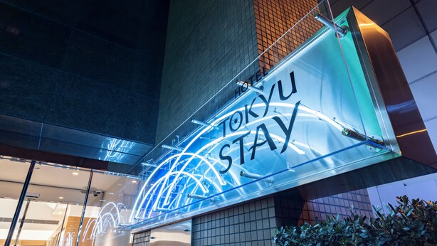 Letreiro de neon com a inscrição 'Tokyo Stay' na fachada de um prédio.