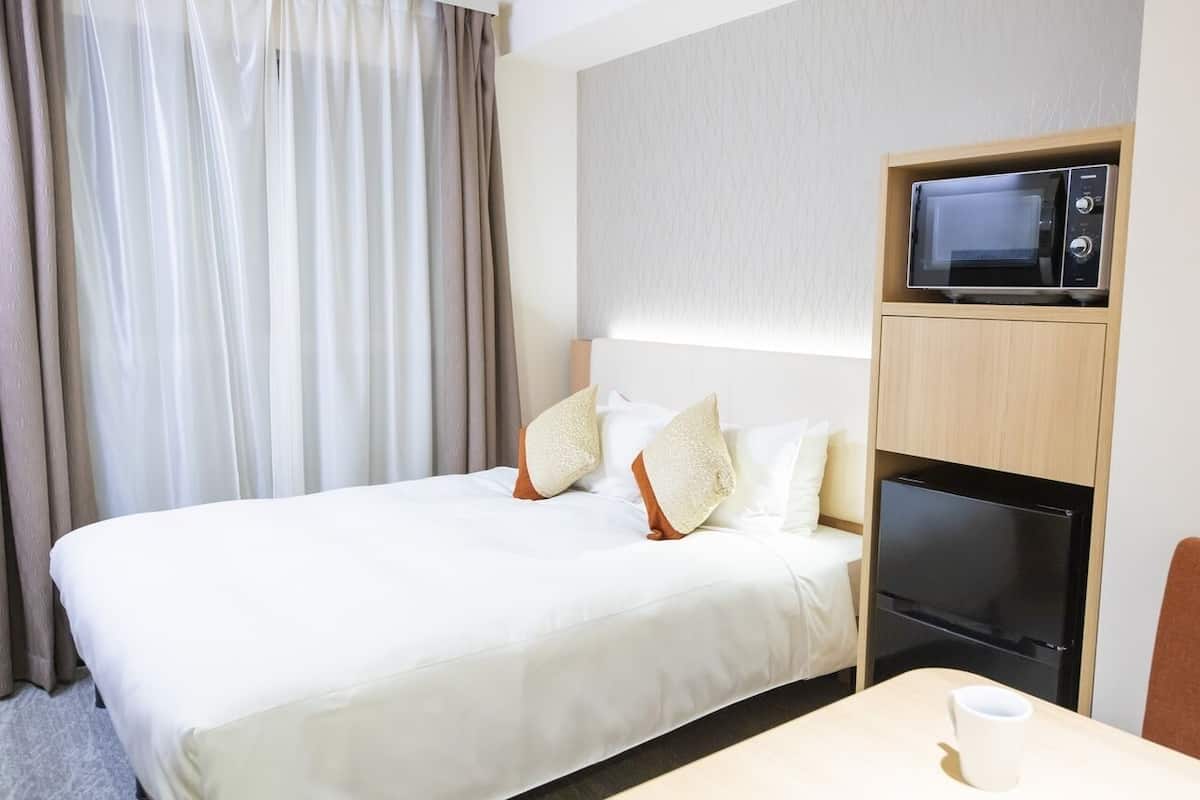 Ein Hotelzimmer mit Bett, einer Mikrowelle, einem Kühlschrank, einem Tisch mit einer Tasse und einem Sessel.