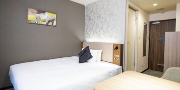 A hotel room with a bed, a desk, a wall-mounted artwork, a patterned wall, and a wooden door.