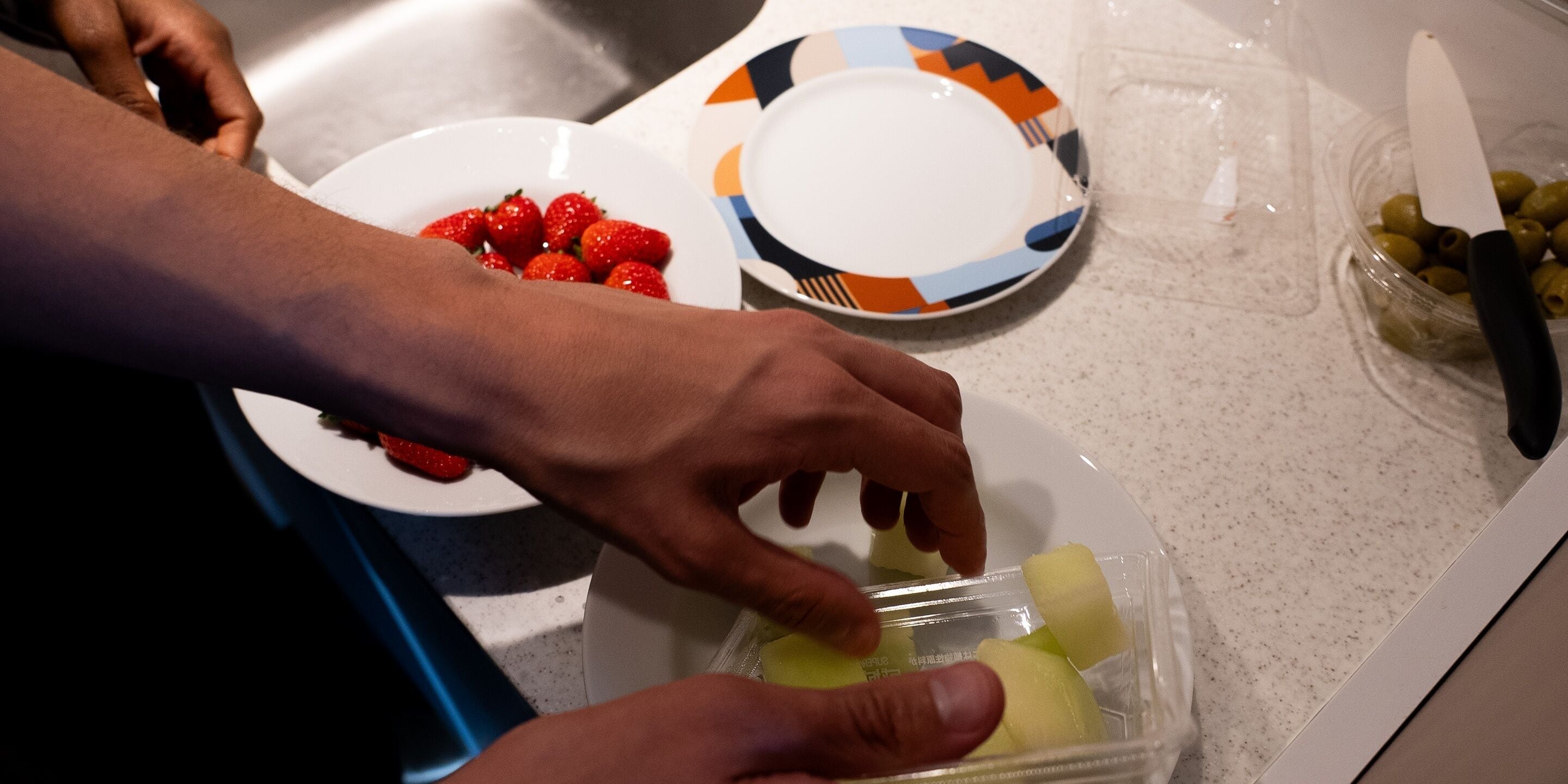 A person preparing food with strawberries and a plastic container.