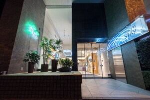 A hotel entrance with a neon sign, potted plants, and a tiled walkway.