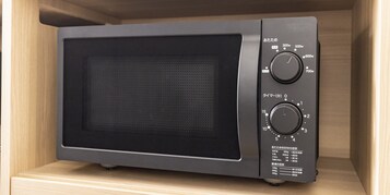 A microwave oven with two dials and a digital display, placed inside a wooden cabinet.