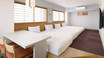 Quarto de hotel com cama, escrivaninha, cadeiras, janela com persianas e ar condicionado.