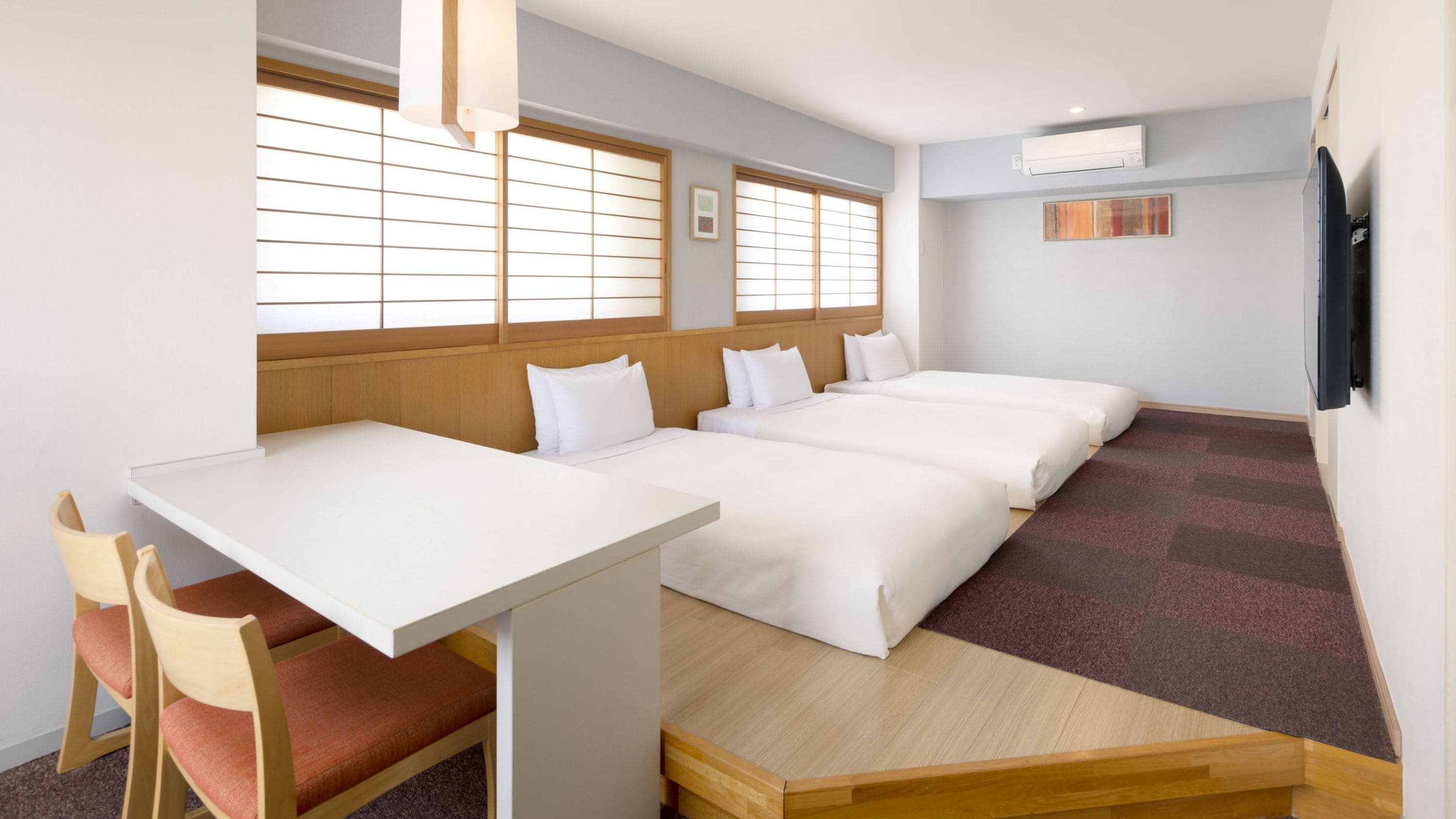 A hotel room with a wooden desk, two beds, a chair, and large windows.