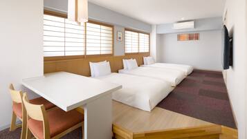 A hotel room with a wooden desk, two beds, a chair, and large windows.