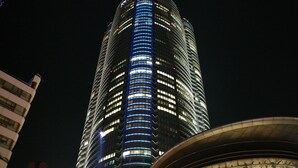 A tall, illuminated skyscraper with a curved facade and a prominent blue-lit central column. - Tokyu Stay Monzen Nakacho Tokyo (Tokyo)