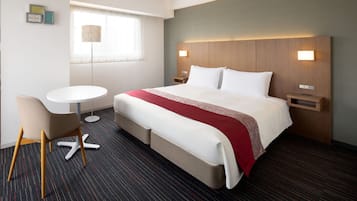 Una habitación de hotel con cama, mesitas de noche, un escritorio y una silla.