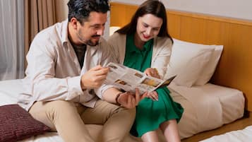 A couple sitting on a bed with a wooden headboard, reading a magazine.