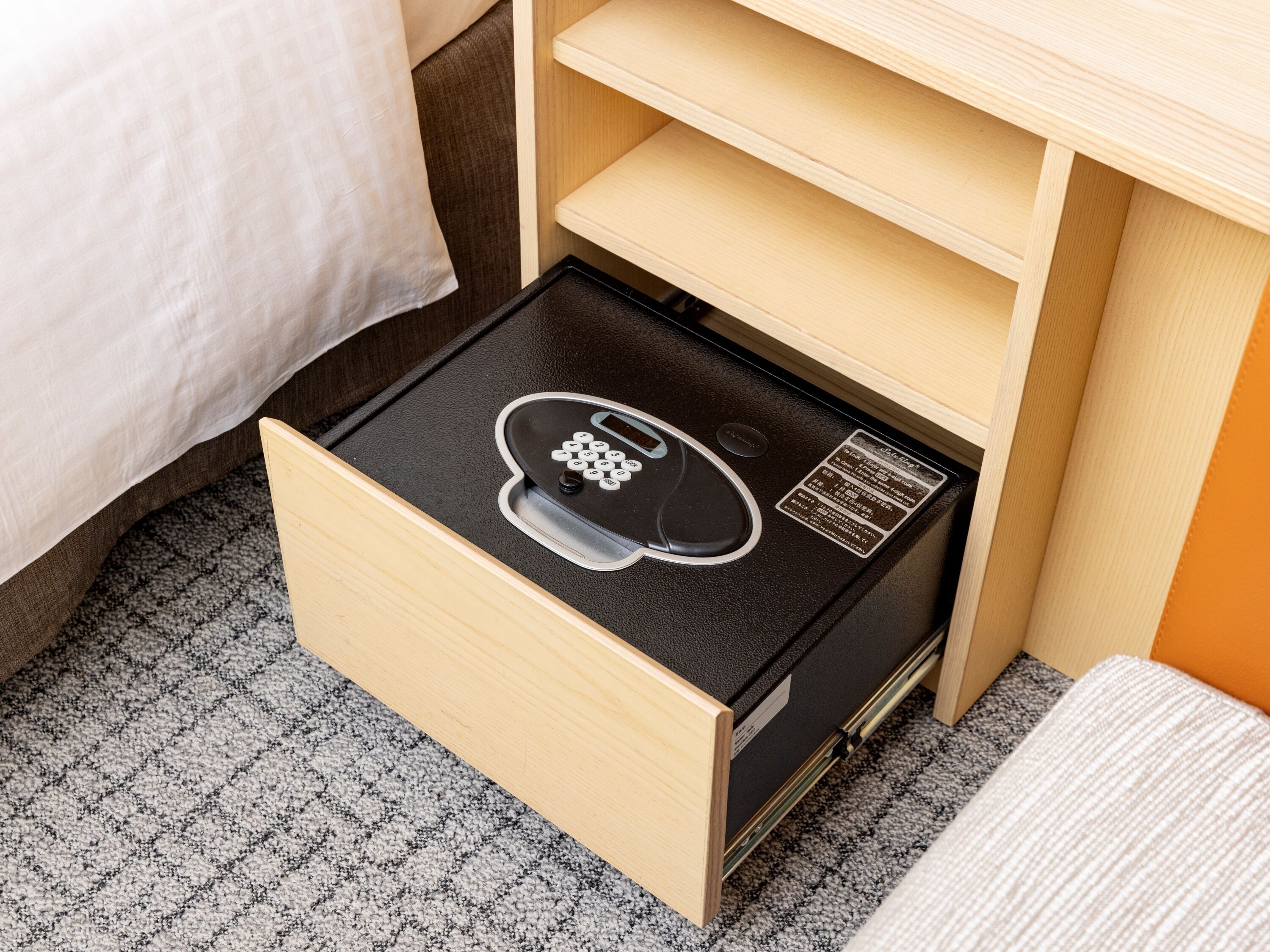 Ein Hotelzimmer mit einem hölzernen Schreibtisch, einem schwarzen elektronischen Gerät auf dem Boden und einem gemusterten Teppich.