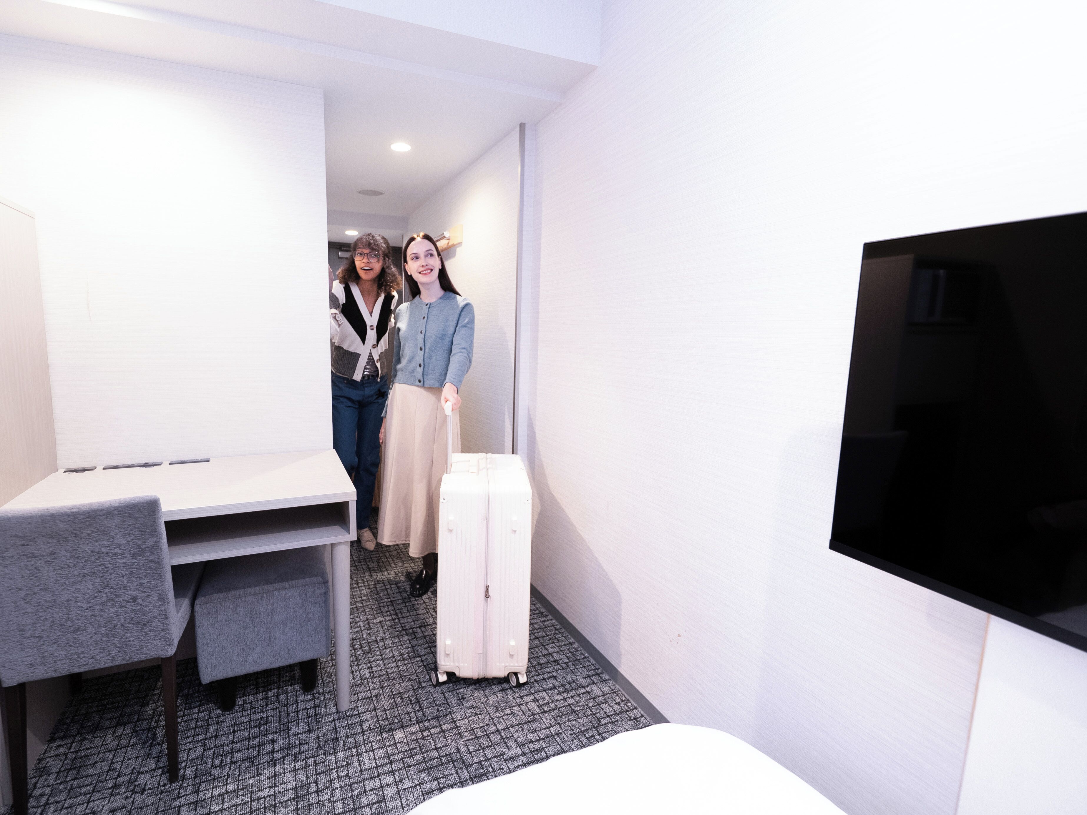 A hotel room with a desk, a TV, and a suitcase.