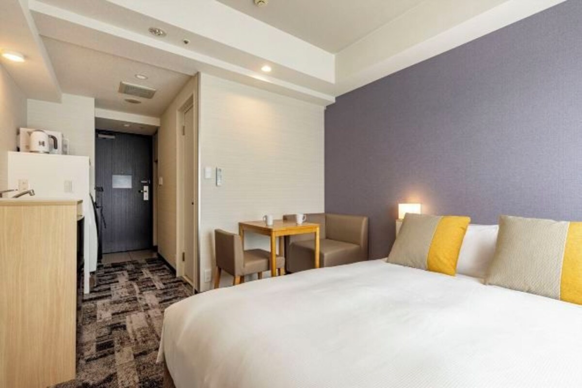 A hotel room with a large bed, a desk with a chair, and a small table with two chairs.