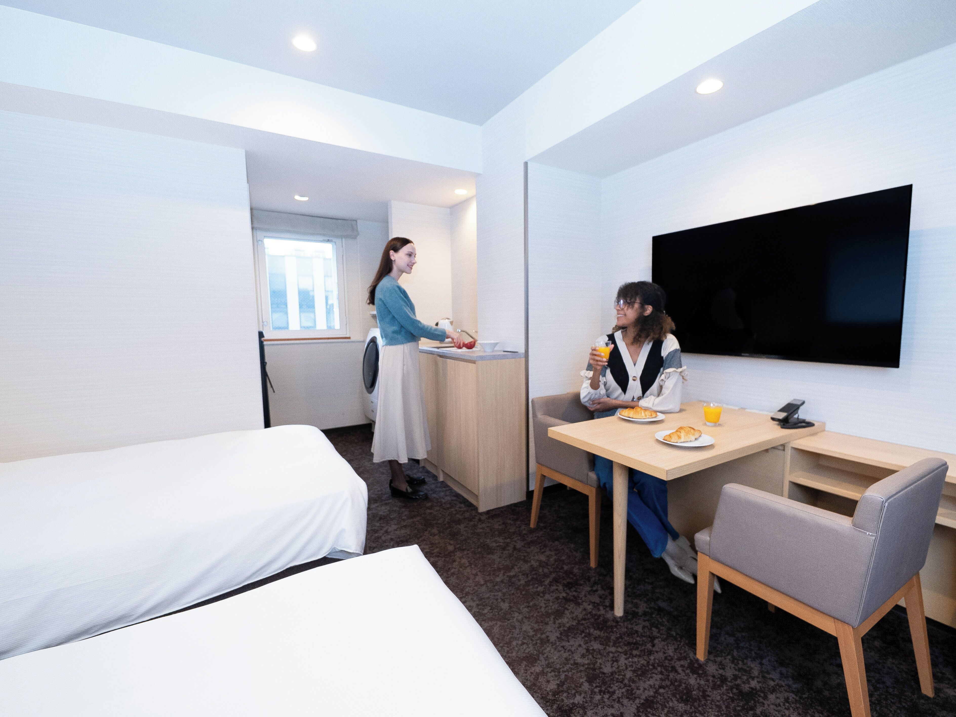 A hotel room with a bed, a desk, a chair, a TV, and a washing machine.