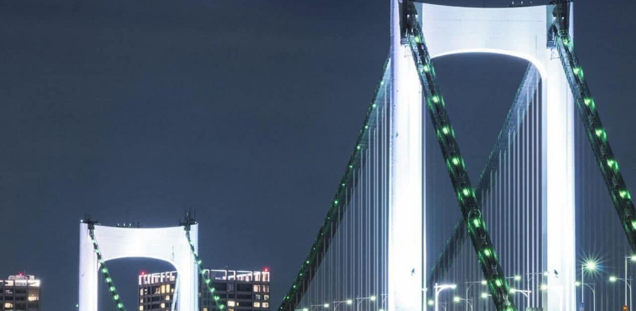 A large suspension bridge at night with illuminated green lights.