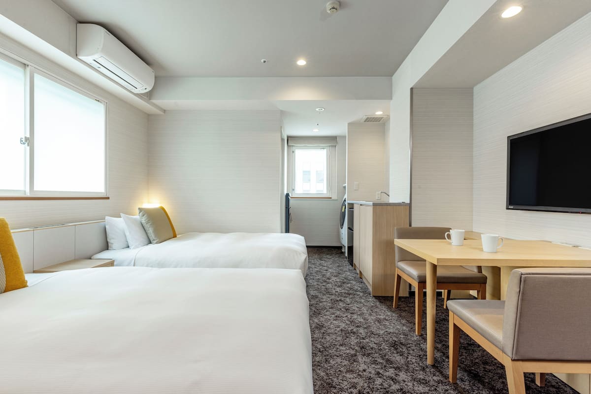 A hotel room with two beds, a desk, a chair, a TV, and a washing machine.