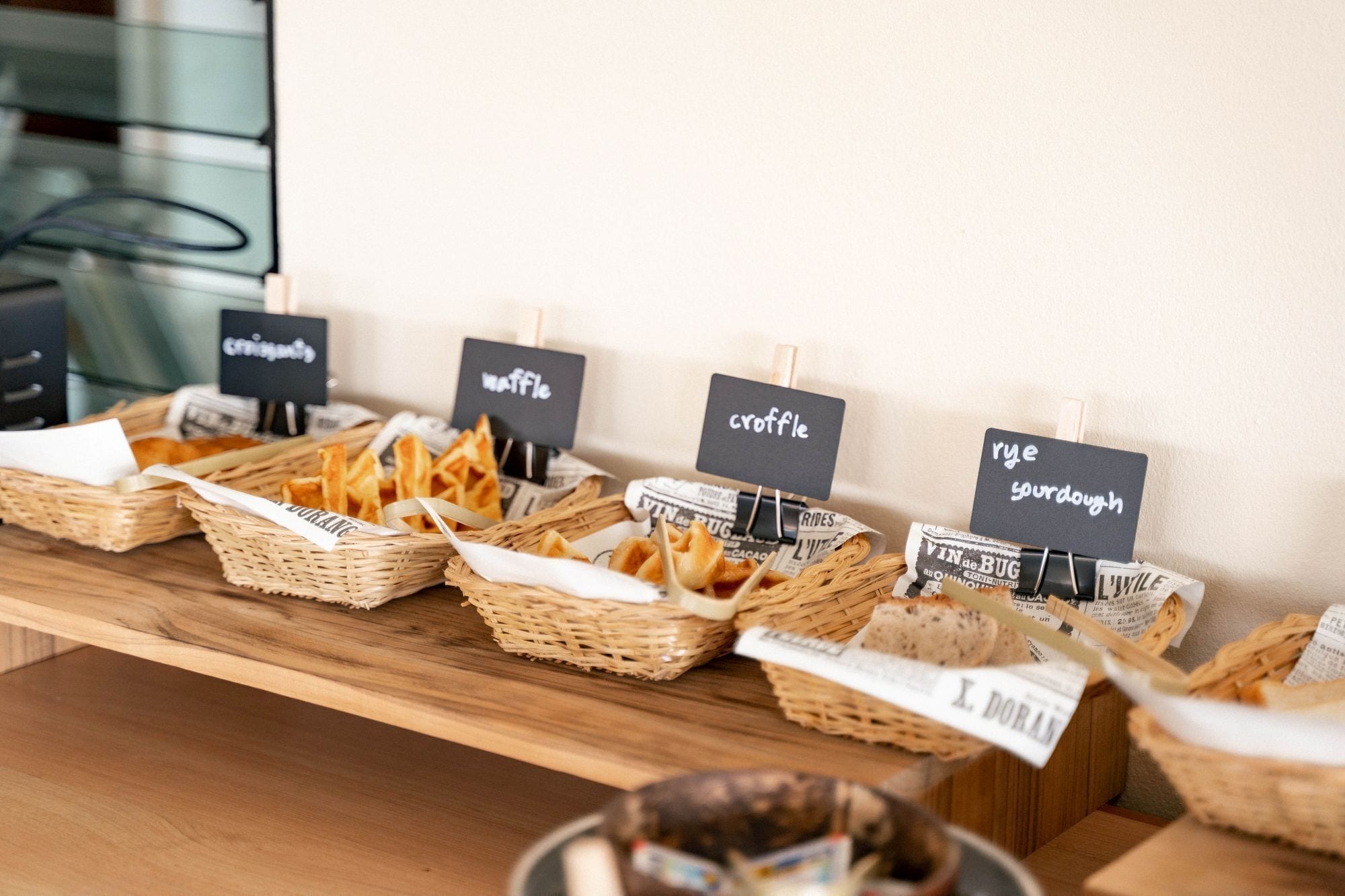 Una mesa de bufé con cestas que indican diferentes tipos de comida, como croquetas, gofres y pan de centeno.
