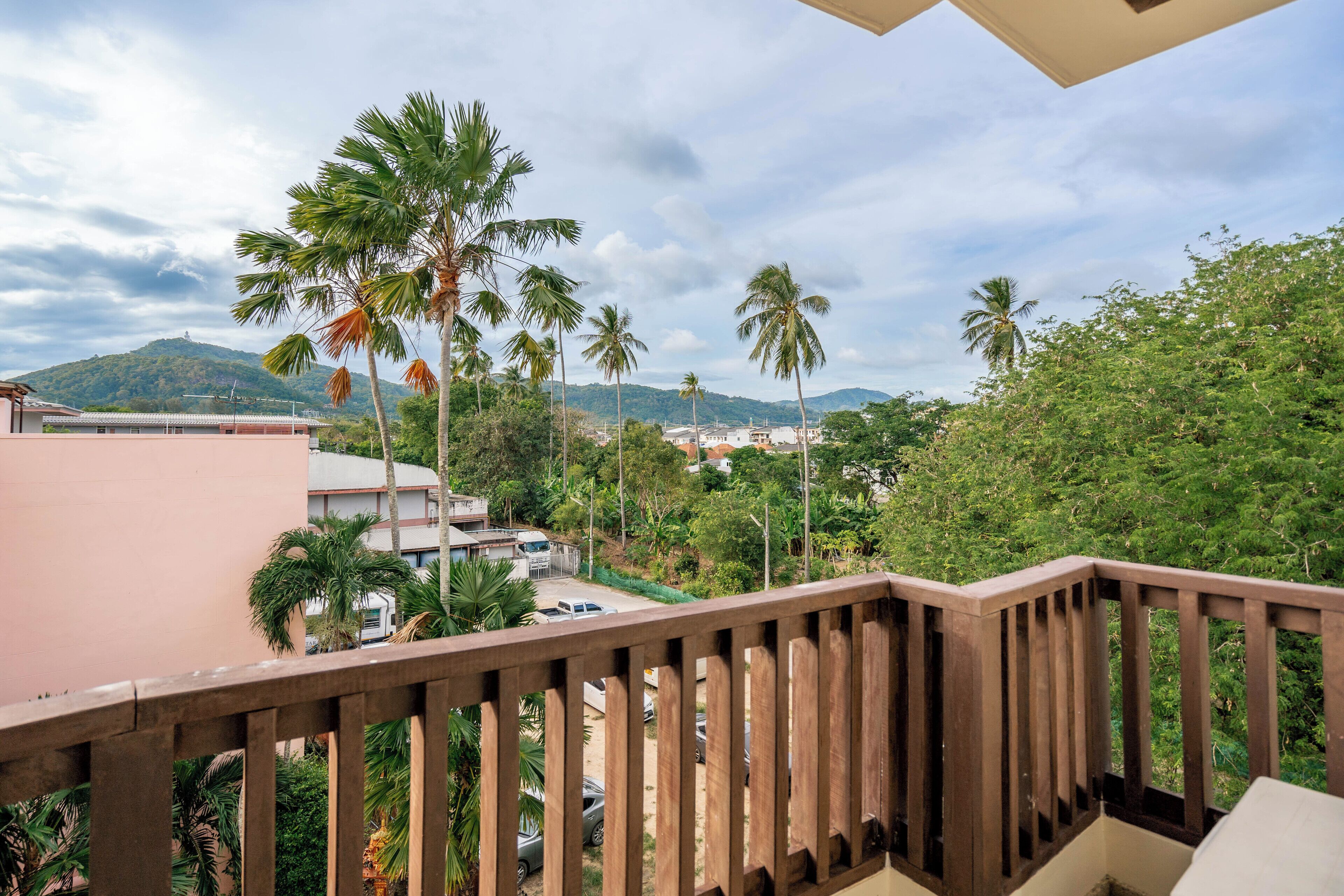 A balcony with a wooden railing overlooking a residential area with palm trees and houses.