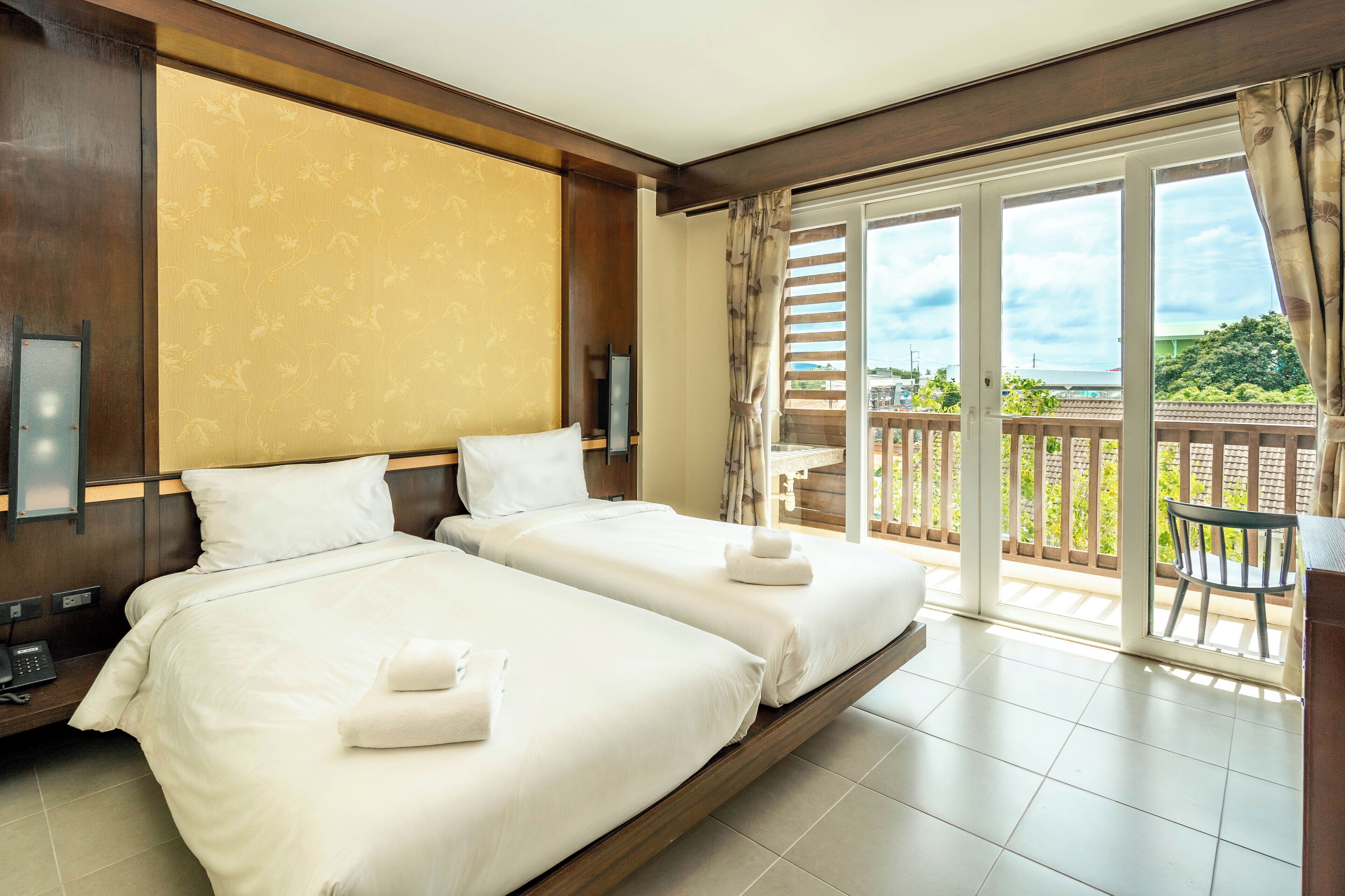 A hotel room with two beds, a balcony with a view, and a wooden floor.
