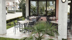 An outdoor patio area with tables and chairs, a large window, and a potted plant. - Ganfo (Sirmione)