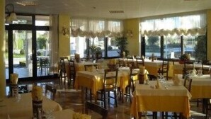 A dining area with tables set for service, large windows with curtains, and a view of the outdoors. - Ganfo (Sirmione)