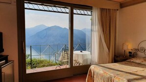 A bedroom with a bed, a nightstand, a lamp, and a view of mountains through a large window.