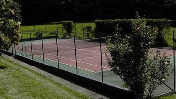 Ein Tennisplatz, umgeben von einem Metallzaun und üppigem Grün.