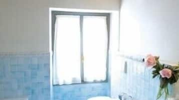 Ein Badezimmer mit Badewanne, Toilette und Waschbecken. Ein Fenster mit Vorhängen, und die Wände sind mit Fliesen versehen.
