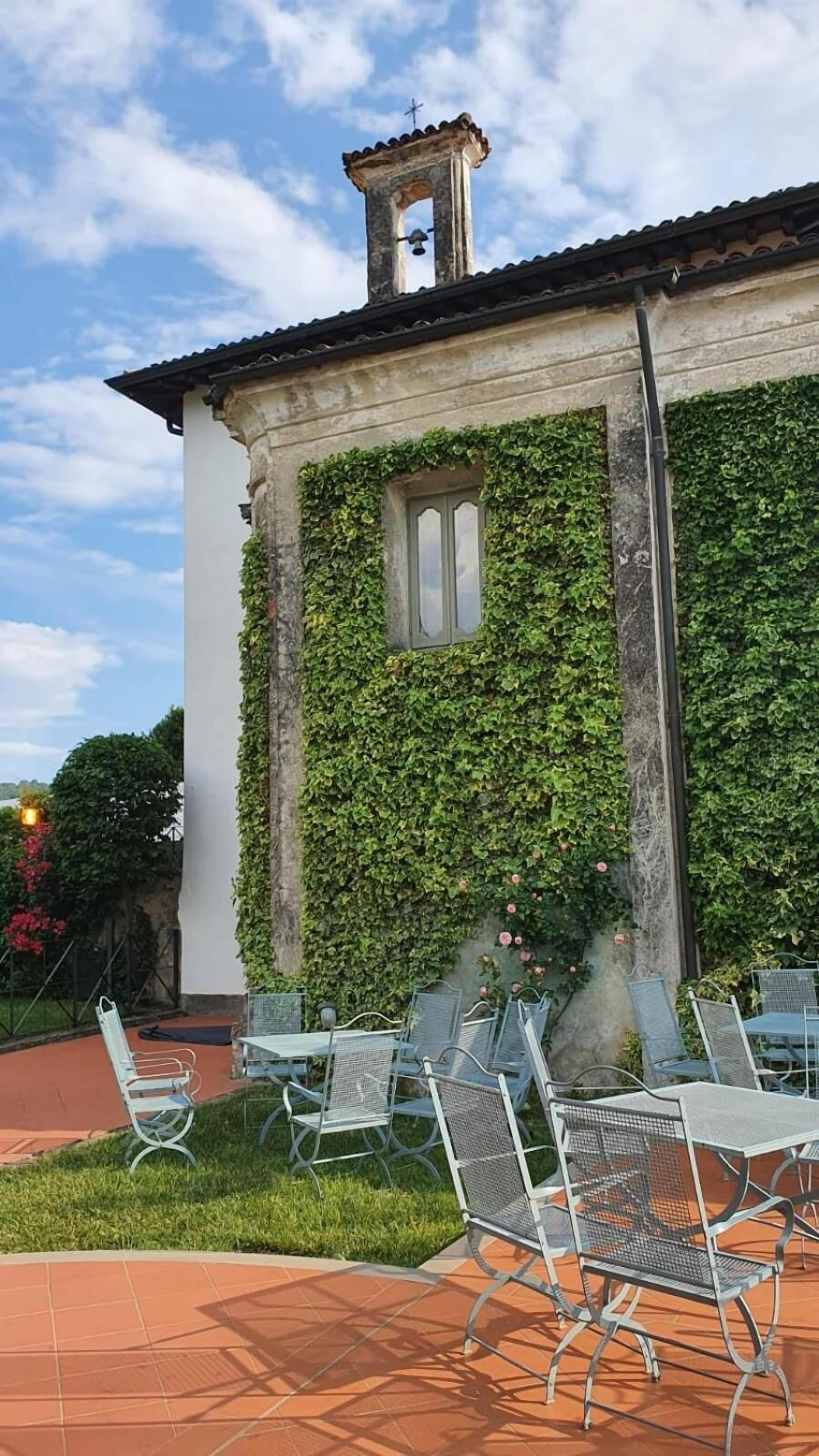 A building with a bell tower, ivy-covered walls, and outdoor seating with metal chairs and tables.