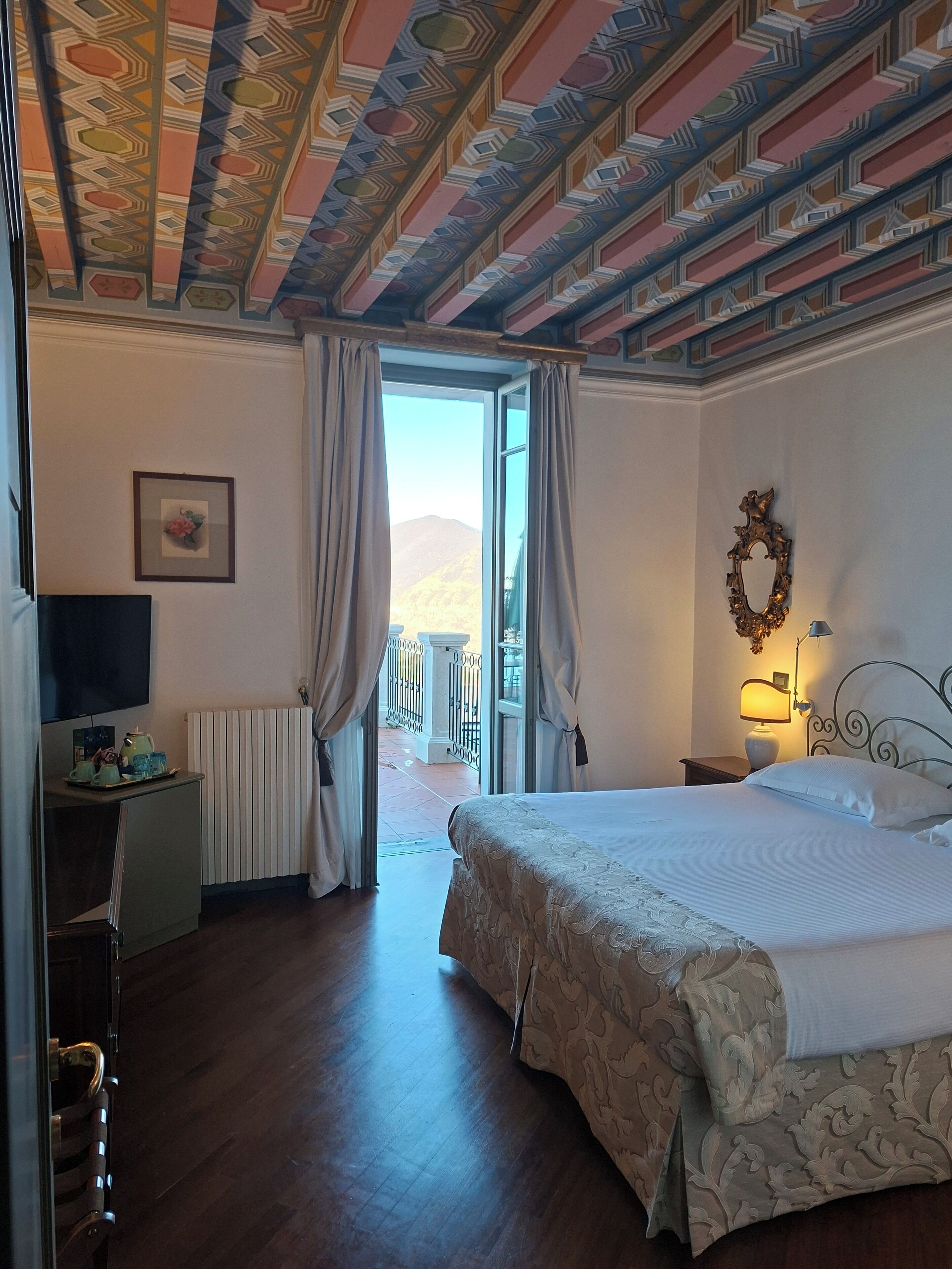 Une chambre d’hôtel avec un grand lit, un bureau avec un ordinateur, une fenêtre avec des rideaux et un plafond décoratif.
