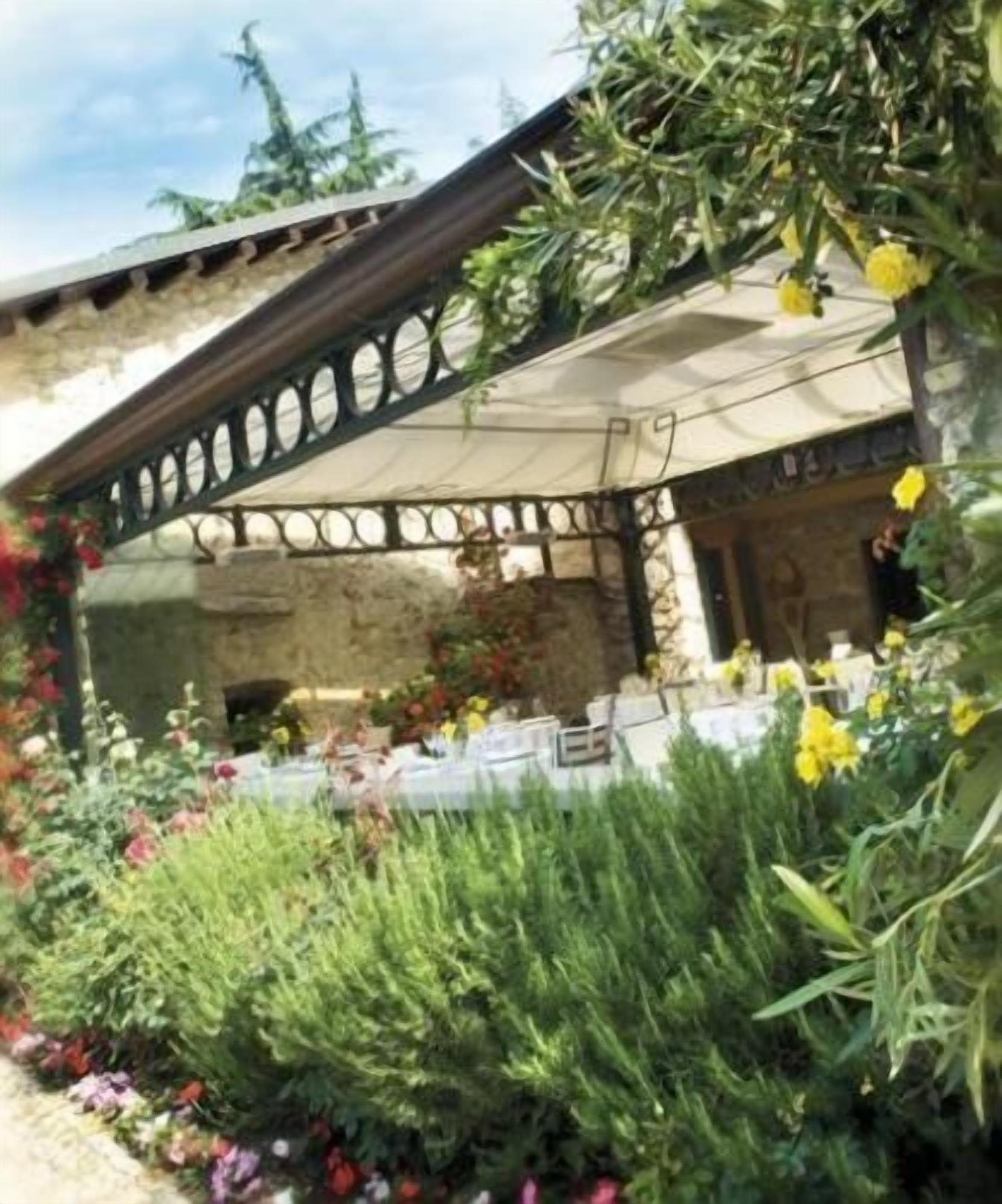 An outdoor seating area with tables and chairs, surrounded by lush greenery and flowers.