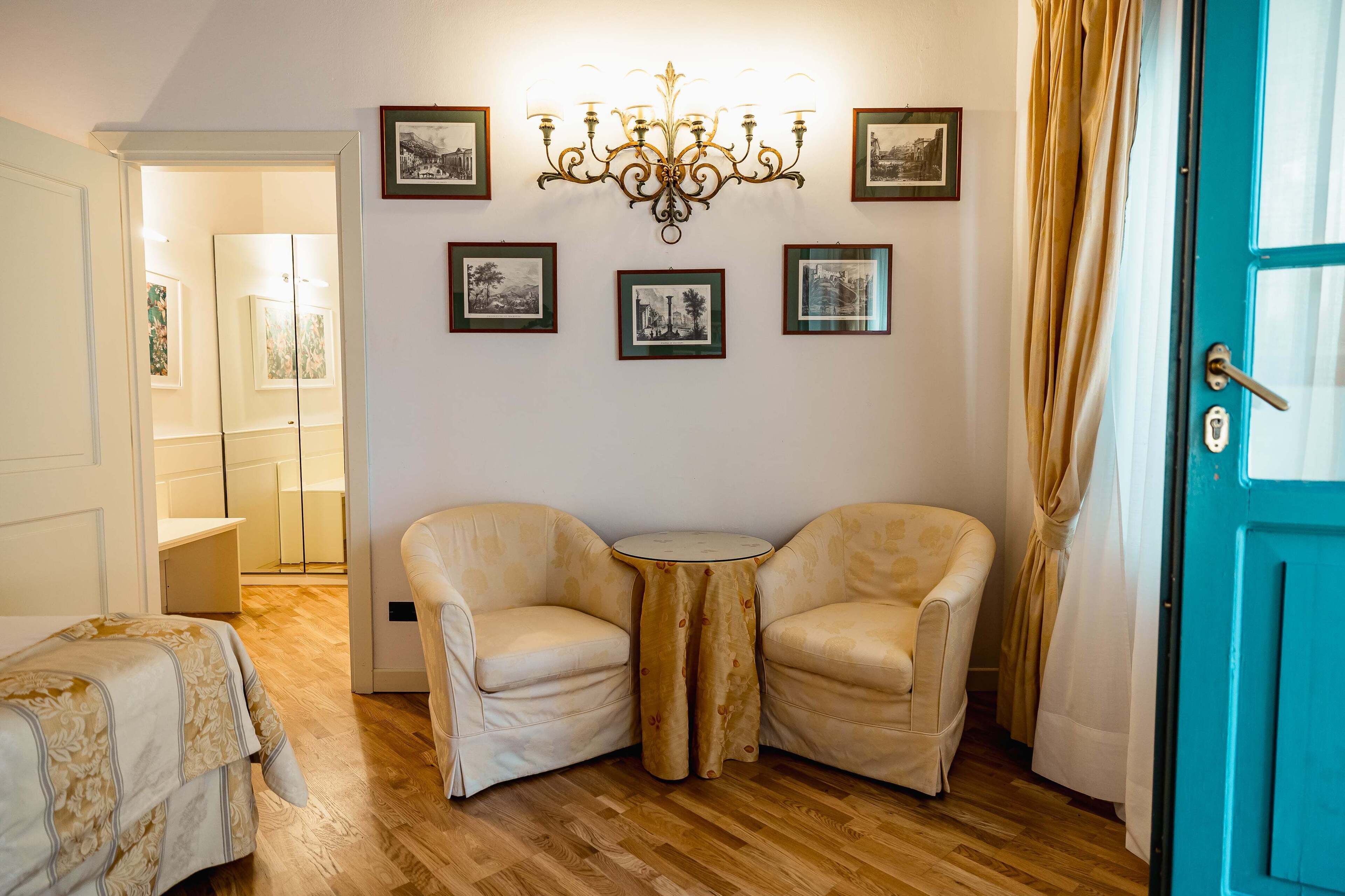A room with a wooden floor, two beige armchairs, a small round table, a blue door, and a chandelier.