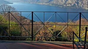A terrace with a metal railing overlooking a lake and mountains.