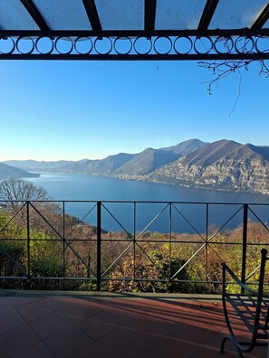 A terrace with a metal railing overlooking a lake and mountains.