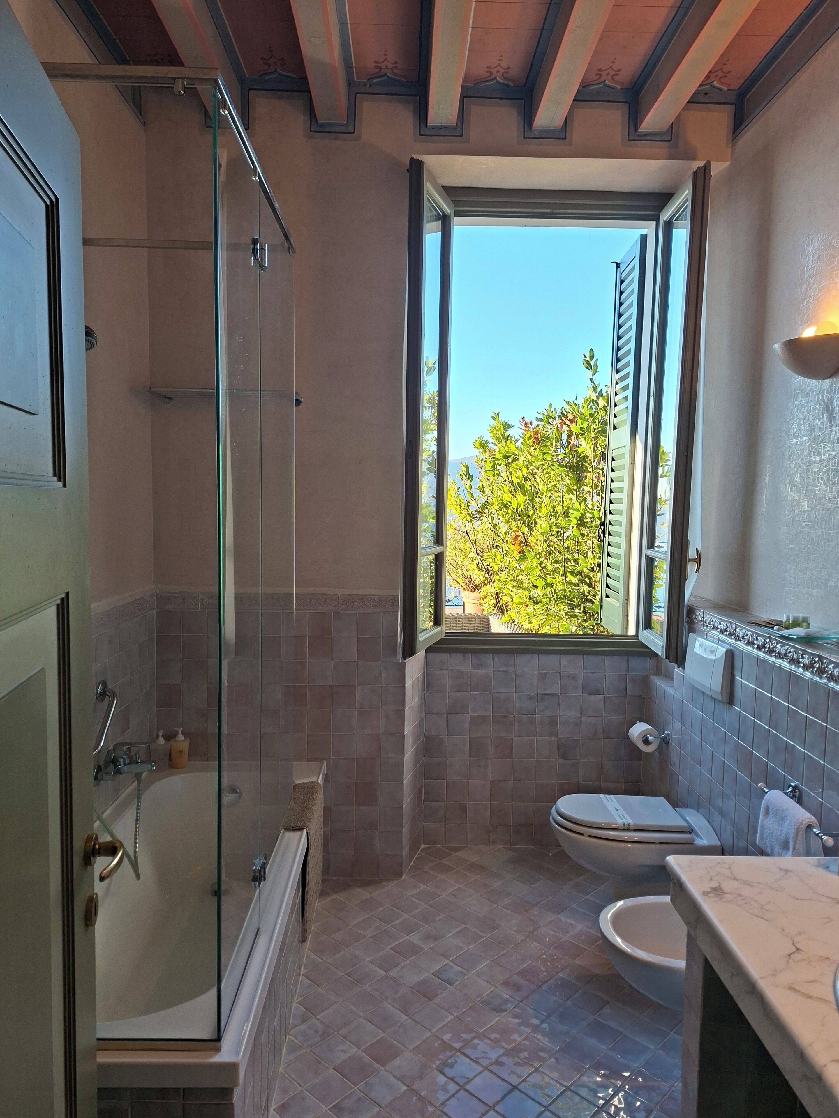 Un baño con ducha compartimentada por vidrio, un inodoro y un lavamanos con encimera de mármol.