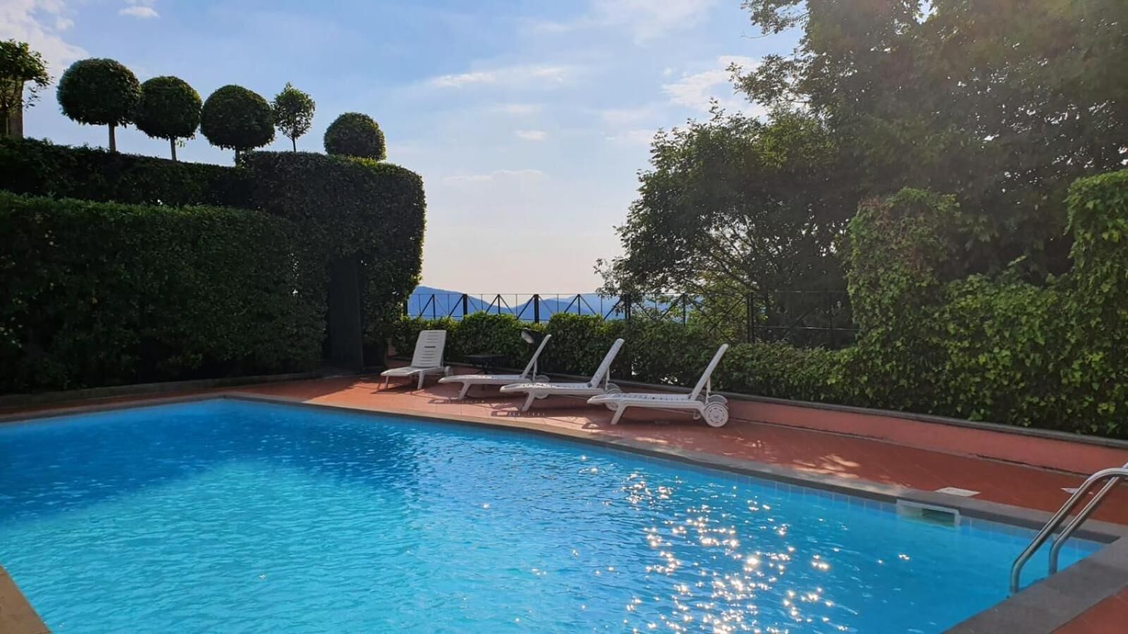A swimming pool with lounge chairs and neatly trimmed hedges.