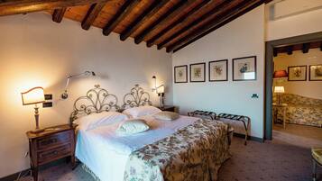 Un dormitorio con techo de madera, una cama con ropa de cama floral, lámparas de noche y cuadros en la pared.