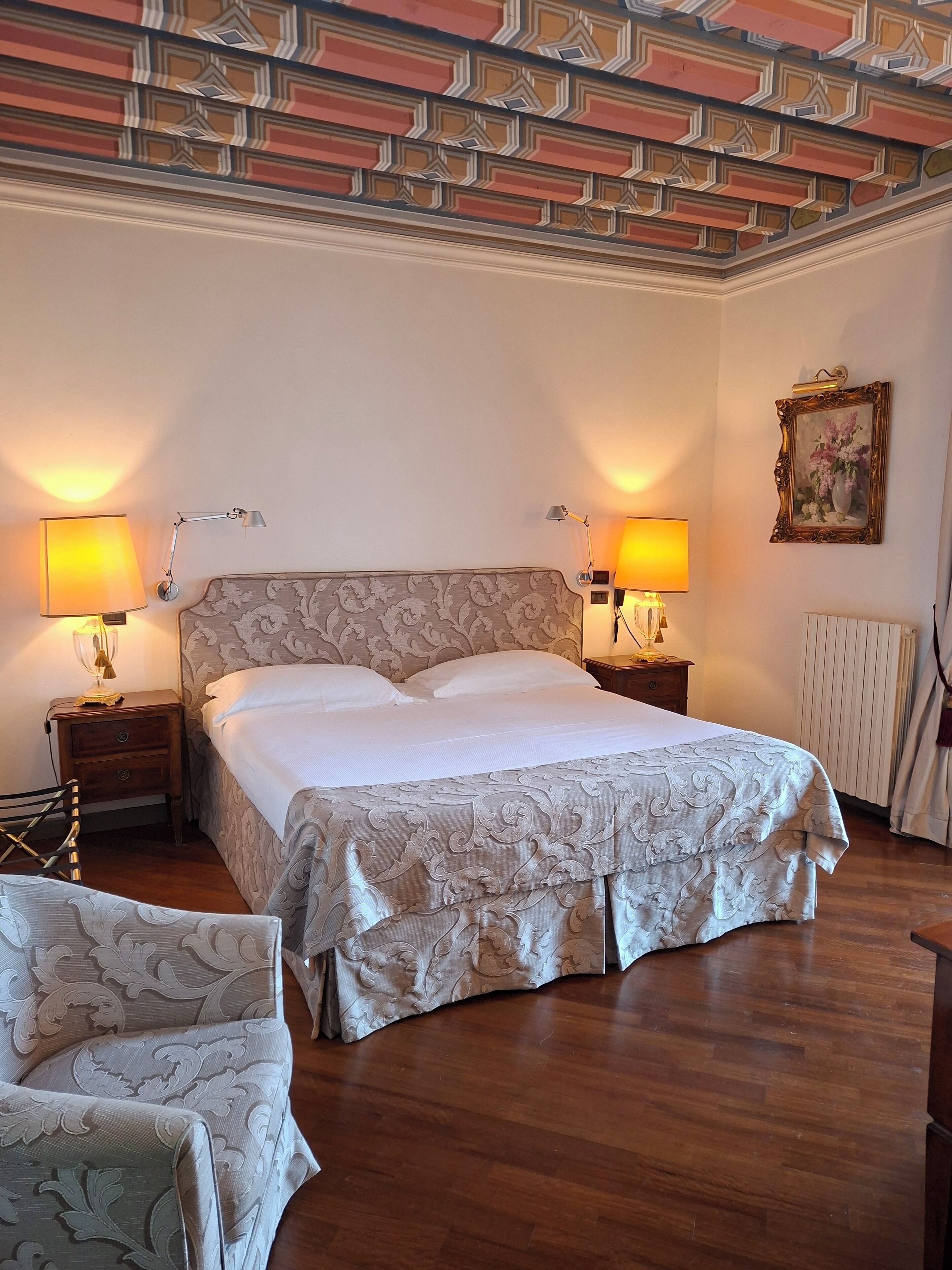 Ein Schlafzimmer mit einem großen Bett, zwei Nachttischlampen, einem Sessel und einer dekorativen Decke.