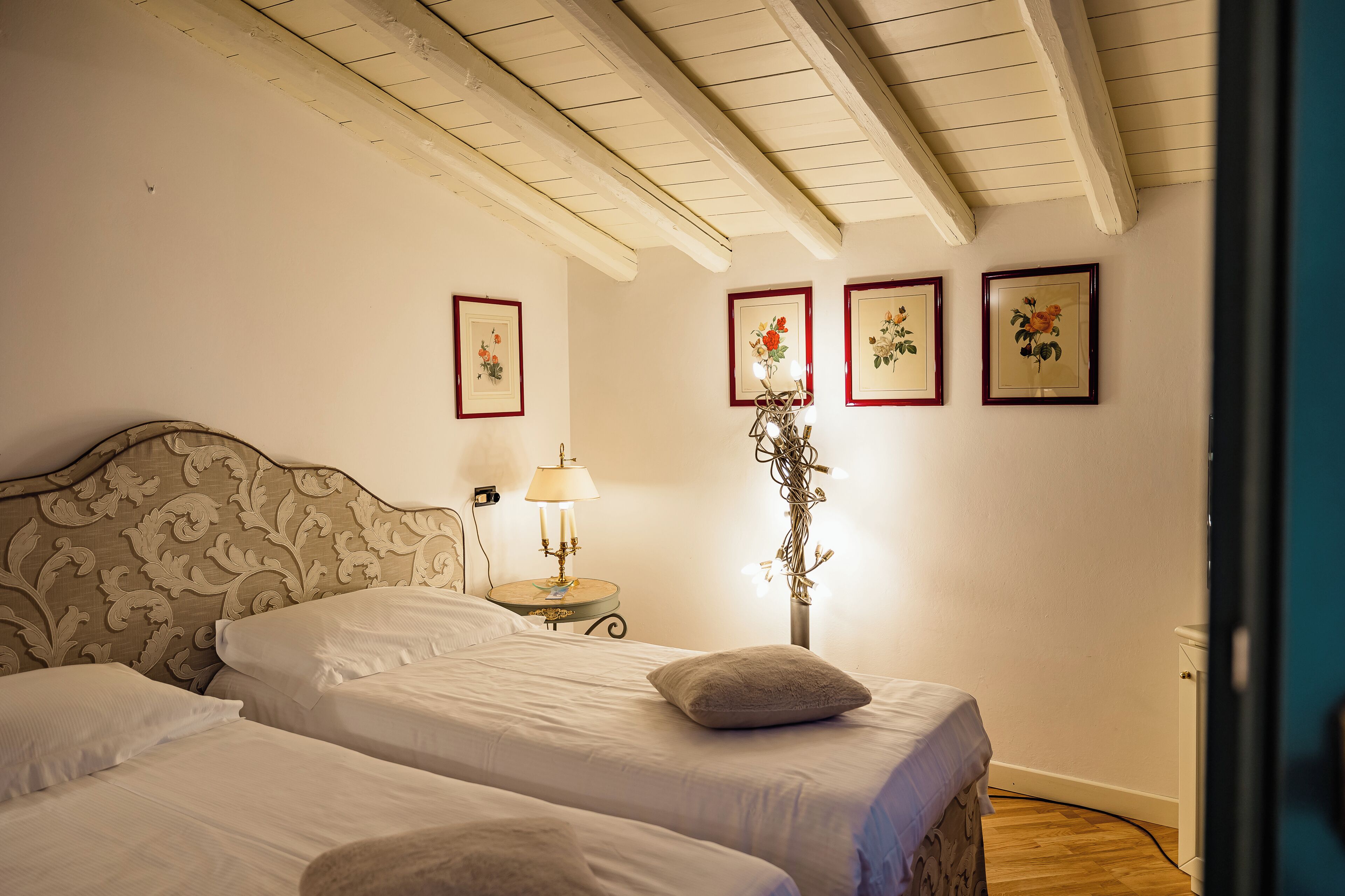 Un dormitorio con dos camas, una mesita de noche con lámpara y decoración floral en la pared.