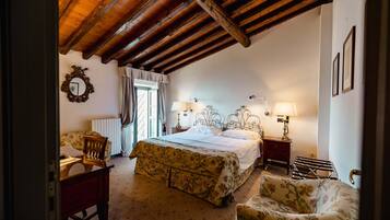 Une chambre avec un plafond en bois, un lit recouvert d’une couette à motifs floraux, deux lampes de chevet, une chaise et un radiateur.
