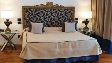 A hotel room with a large bed, two bedside tables, a nightstand, and a patterned headboard.