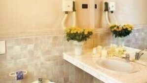 A bathroom with a toilet, bidet, and a sink with a mirror. There are two flower arrangements on the sink counter.