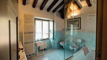 Un bagno con vasca, water e doccia, dotato di finestra e termosifone.
