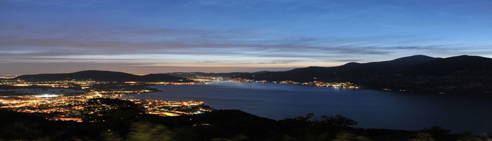 Un paisaje urbano costero al atardecer, con vista al mar y montañas lejanas.