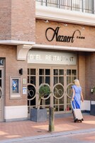 A hotel restaurant named "Nazaert" with a sign above the entrance, a large glass door, and a woman pulling a suitcase.