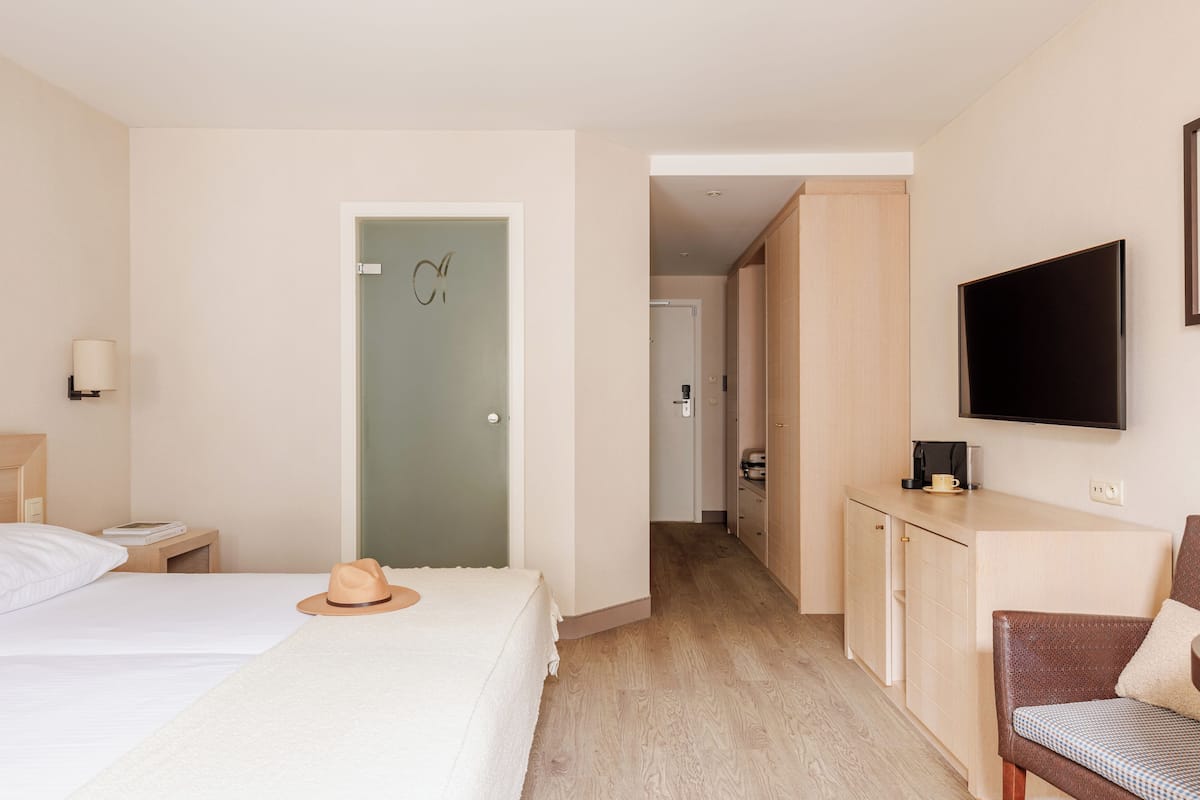 A hotel room with a bed, a desk, a chair, a television, and a door with a sign.