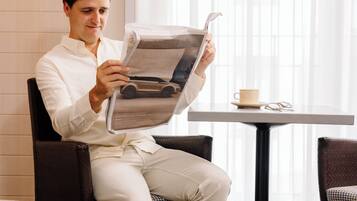 A man sitting in a chair reading a magazine, with a table and a cup of coffee nearby.