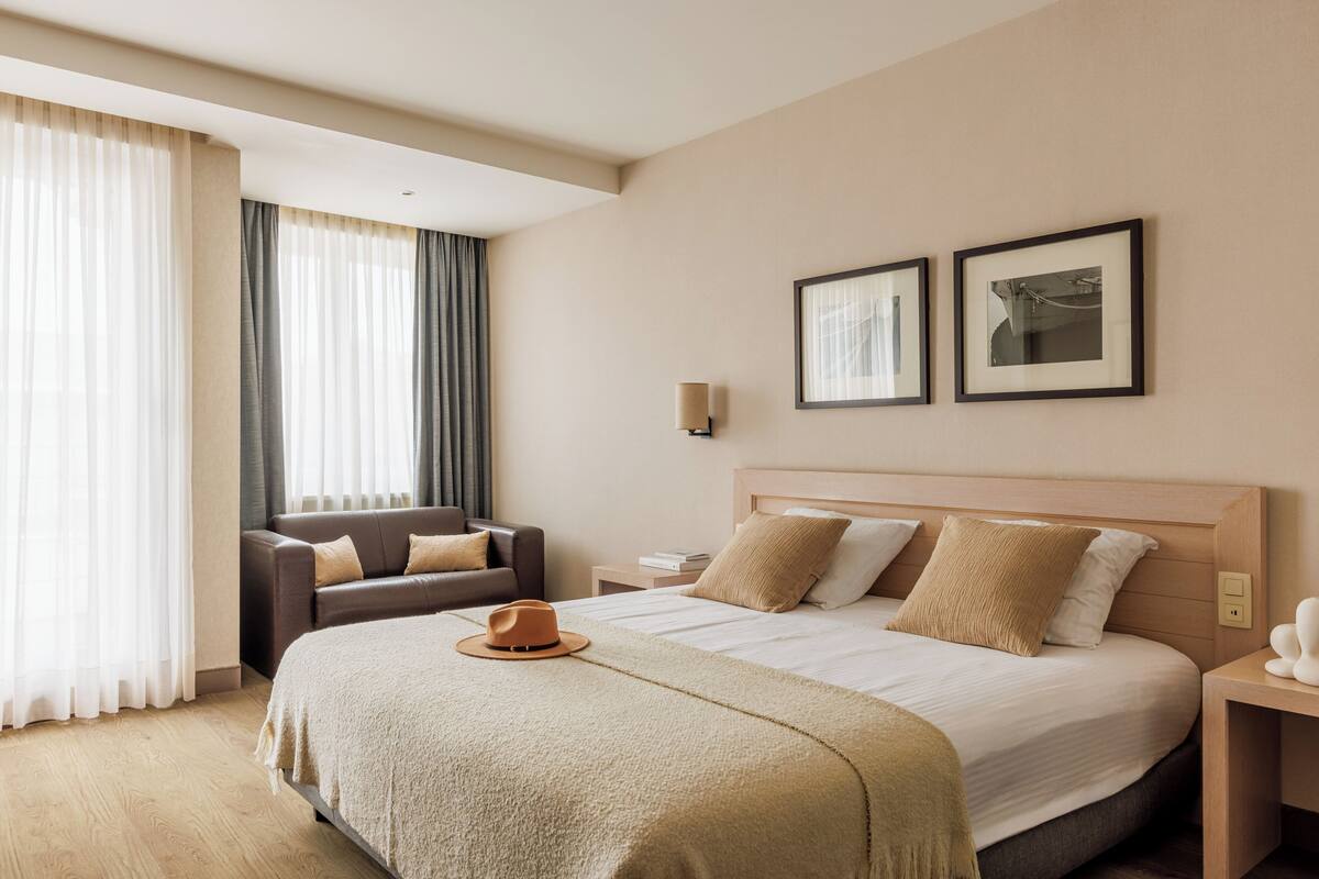 A hotel room with a large bed, a sofa, a nightstand, and a window with curtains.